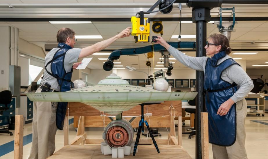 Two people inside the Conservation Lab work to photograph the U.S.S. Enterprise through radiography.