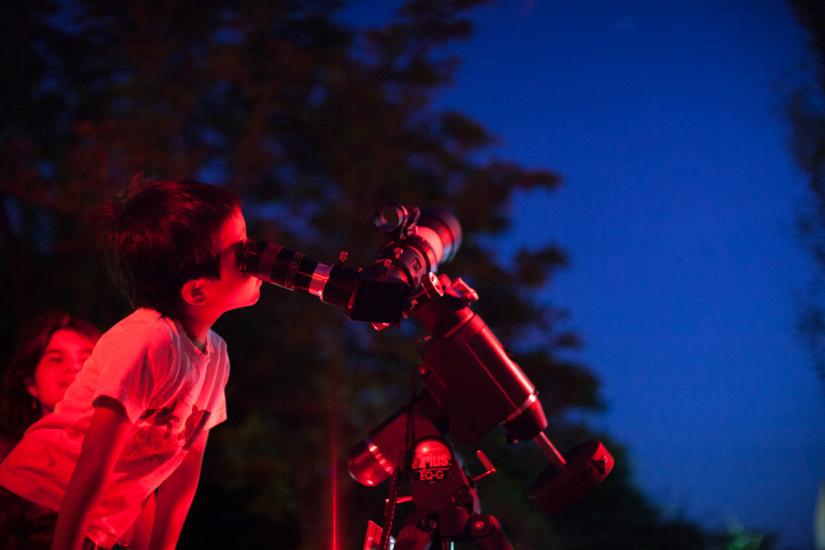 A young person looks through a telescope during a nighttime observing event.