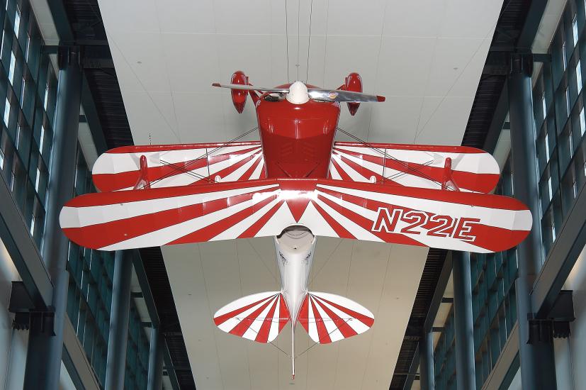 A biplane that hangs upside down, with a red body and red and white striped wings. 