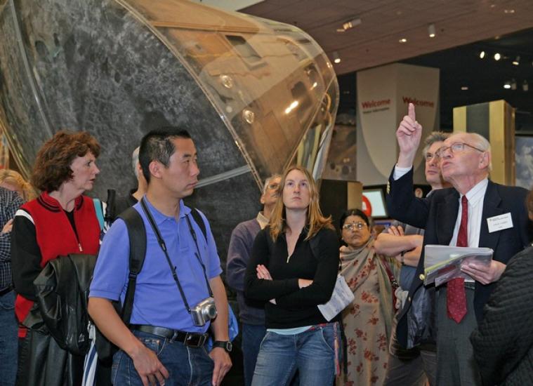 A docent points to an object inside the museum while giving a tour to several people.