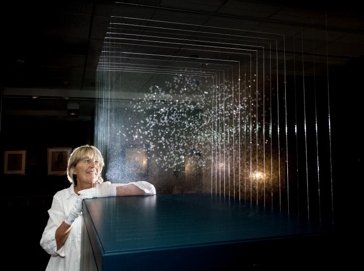 Angela Palmer, a white woman, stands next to the installation of her glass sculpture highlighting the findings of the Kepler Space Telescope.