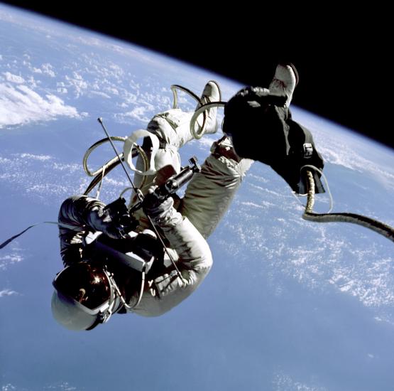 Edward White, a male astronaut, floats in zero gravity with a backdrop of Earth behind him.