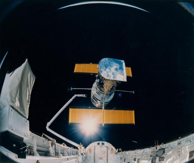 The Hubble Space Telescope, a large telescope with a set of solar panels on two sides, is deployed from the Space Shuttle Discovery.