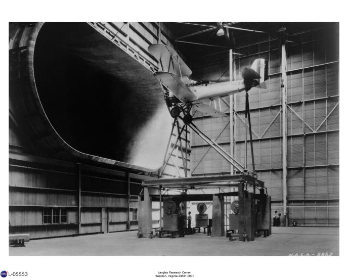 An aircraft on a lift is placed in front of a large oval tunnel in a hangar.