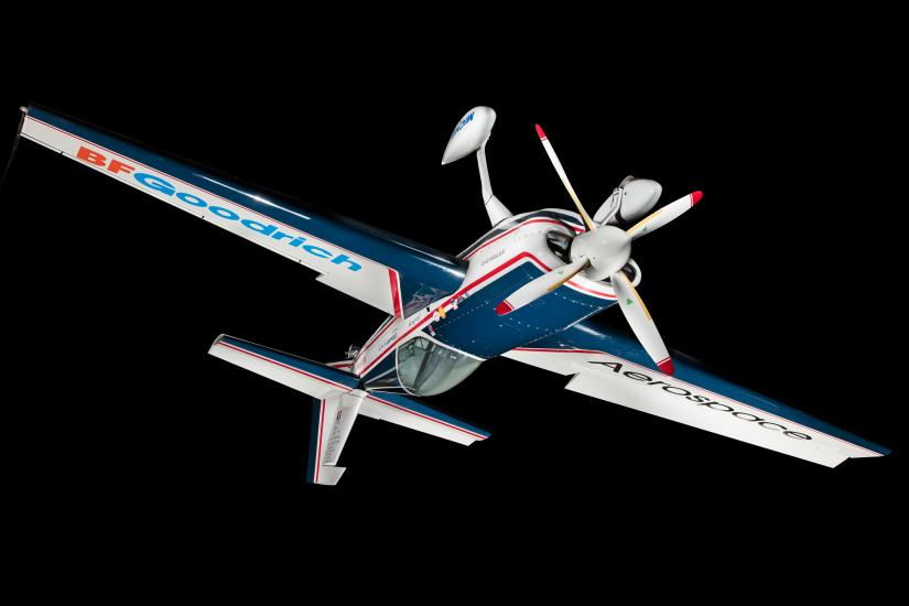 Blue and white monoplane with red trim and sponsor logos, hanging inverted