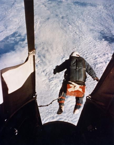 A man jumps out of a gondola of a balloon. You can see him in free fall and the cloud cover below.