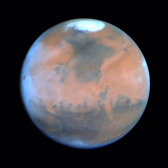 A disk view of Mars, with clouds on the western side of the disk.