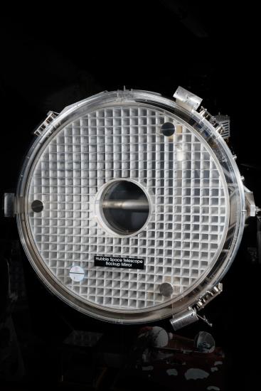 Front view of mirror for use on the Hubble Space Telescope consisting of two layers of glass attached to a thin, square, three-dimensional grid structure. Mirror structure is then placed in a circular frame.