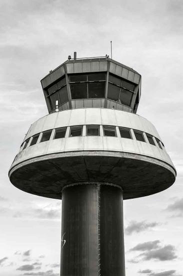 Partial view of an air traffic control tower at Barcelona El-Prat Airport. This tower features a dark-colored cylinder base with a conical-shaped first floor. A second floor features at least four different perspectives for observation.