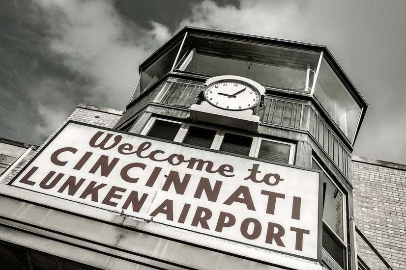 Front view of an air traffic control tower at Cincinnati Municipal Airport. The base is mostly not visible but a sign stating "Welcome to Cincinnati Lunken Airport" is placed under the windows. Above the windows, a clock is visible.