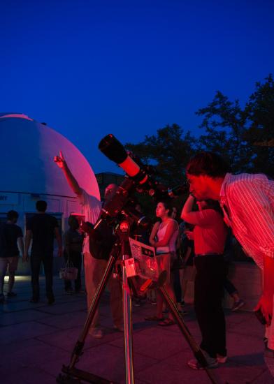 Museum visitors view planets from a telescope during nighttime hours.