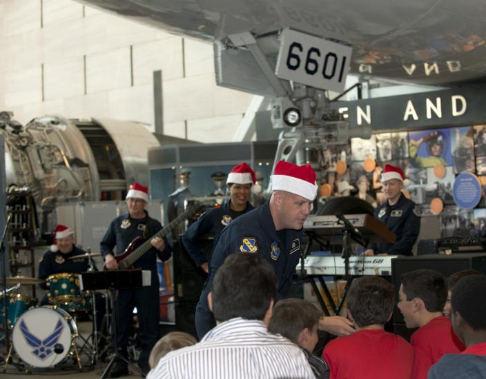 A group of U.S. Air Force musicians perform at the Museum as part of a band. They are wearing red and white Santa hats.