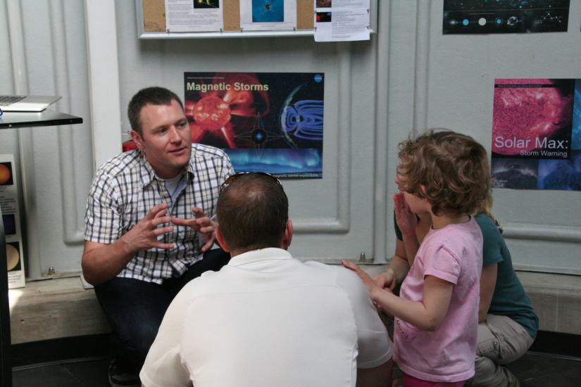 Three museum visitors speak live with an white male expert on astronomy inside the museum's public observatory.