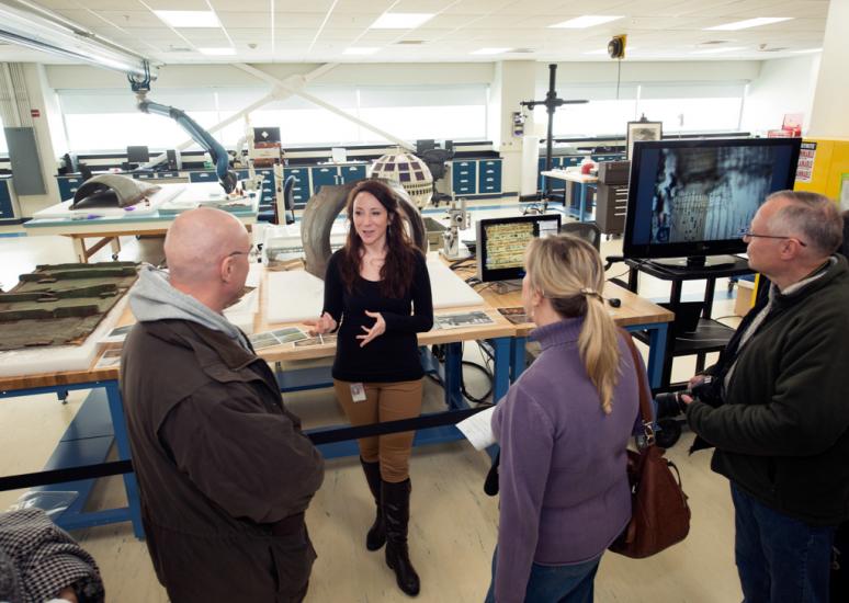 A Museum conservation specialist speaks to three visitors as part of a tour of the Museum's conservation laboratory.