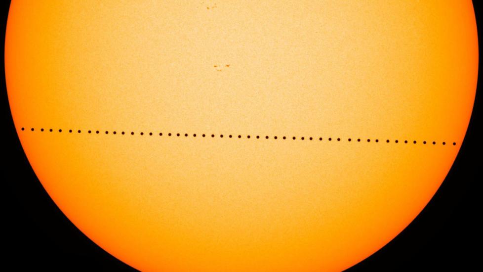 The surface of the Sun with a series of black dots making a line across it; each dot is one image of Mercury's shadow as it crosses in front of the Sun over a period of several hours.