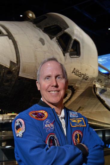 Tom Jones, a white, male NASA astronaut, stands in front of the Space Shuttle Atlantis, a spacecraft, in the Museum's Steven F. Udvar-Hazy Center.