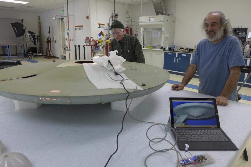 Two Museum specialists test lighting to match the original lighting as part of a gray spaceship studio model used in the Star Trek television series.