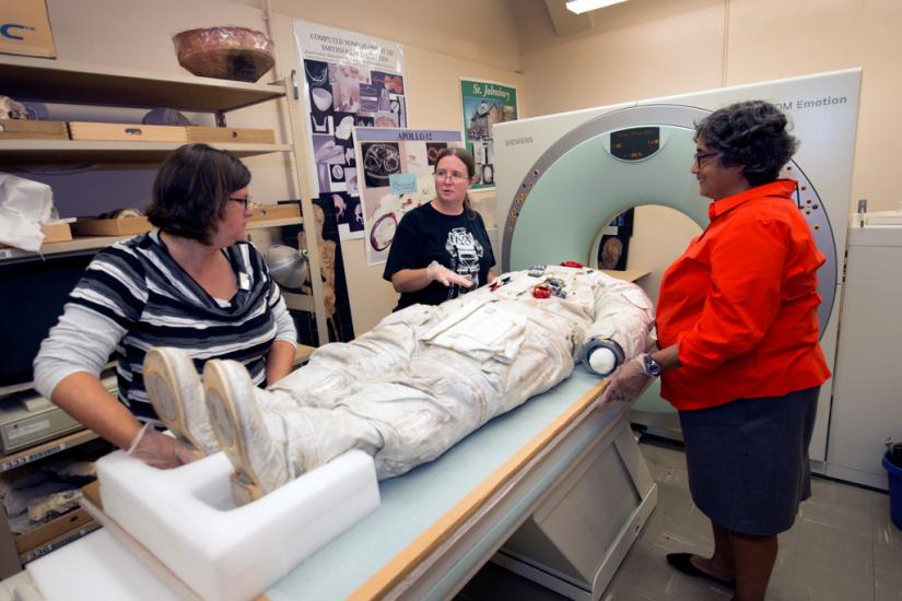 Three Smithsonian staff members prepare Neil Armstrong's spacesuit for a CT scan.