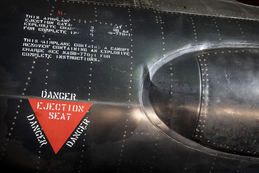 Red triangle "Danger Ejection Seat" label on side of black titanium North American x-15 aircraft