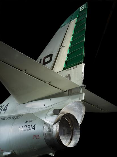 Rear and side view of silver aircraft with green rudder and one engine visible under horizontal stabilizer.