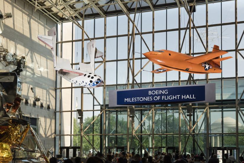 Two airplanes hang from the ceiling in front of a glass wall that has the name "Boeing Milestones of Flight Hall."