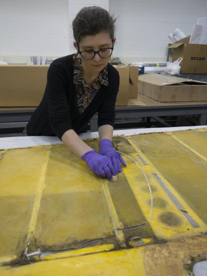 Conservator with purple gloves works over yellow rudder fabric.