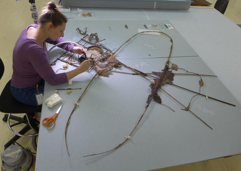 Conservator works over a kite with tools. 