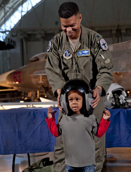 An African-American child has an African-American male member of the Pennsylvania Air Force National Guard place a helmet on his head.