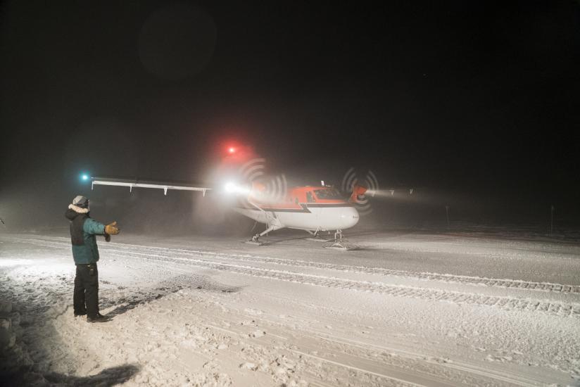 A person gives flight clearance as a orange and white aircraft prepares to leave the frigid continent of Antarctica.