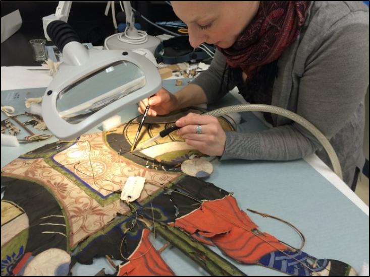 Conservator uses a small tube-like vacuum to clean a kite. 