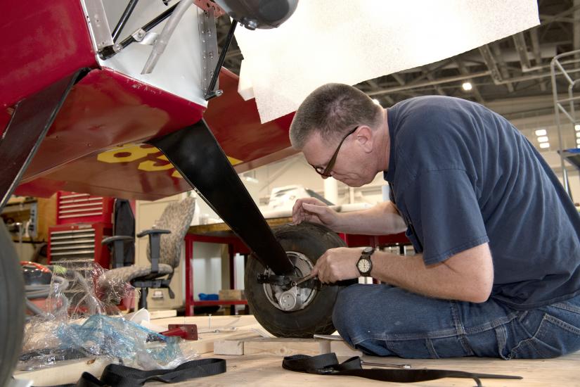 Man sitting on floor working on wheel of red aircraft