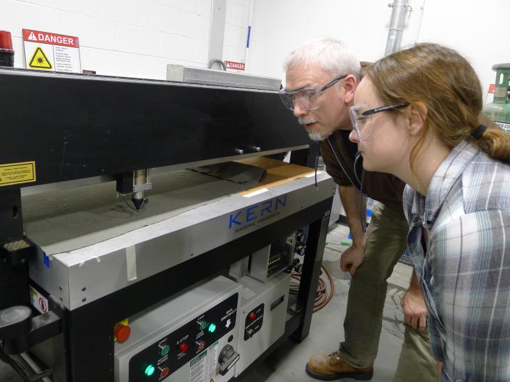 man and woman look at a larger laser cutter