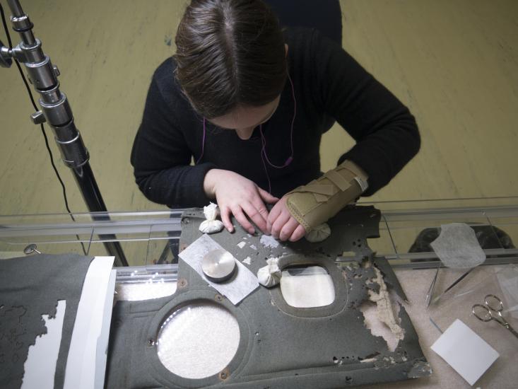 A woman with brace on hand sews gray fabric