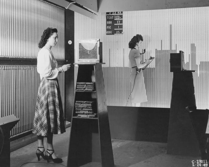 Two women stand at larger boards. 