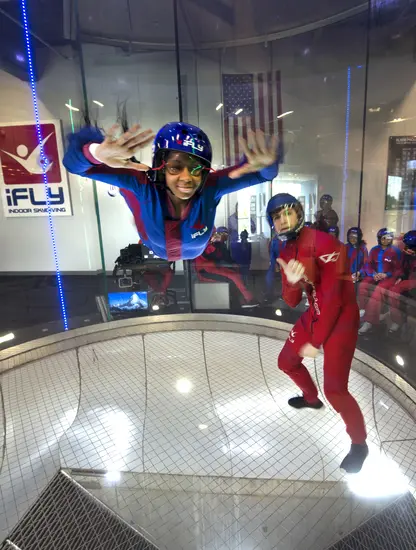 A young girl smiles at the camera will skydiving inside an air tunnel. 