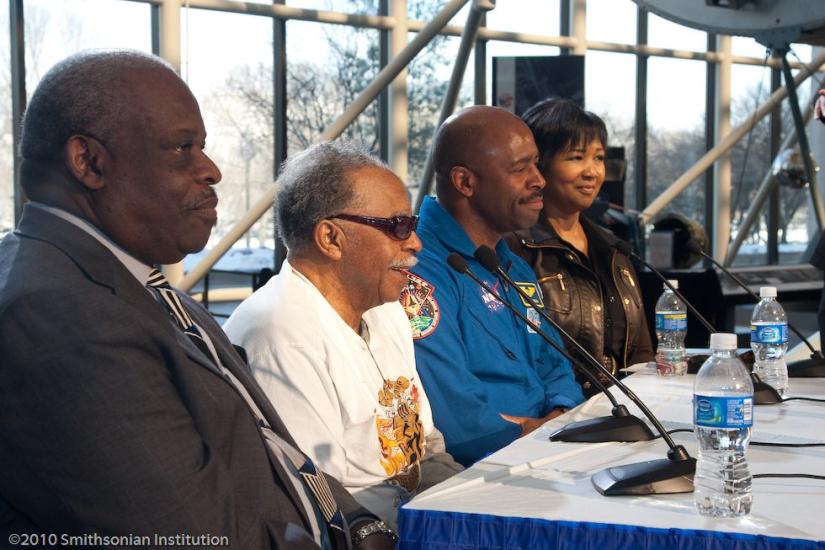 three men and one woman sitting at table with microphones