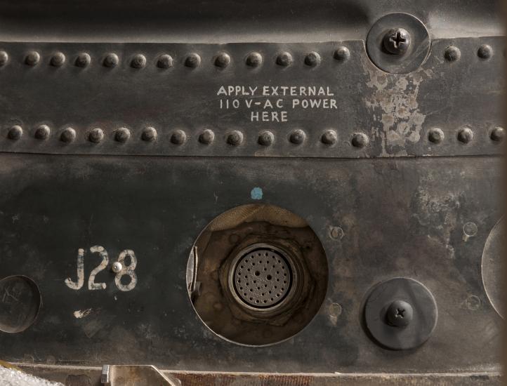 A close up of part of the exterior of the Friendship 7 spacecraft. A plug and notations can be seen.