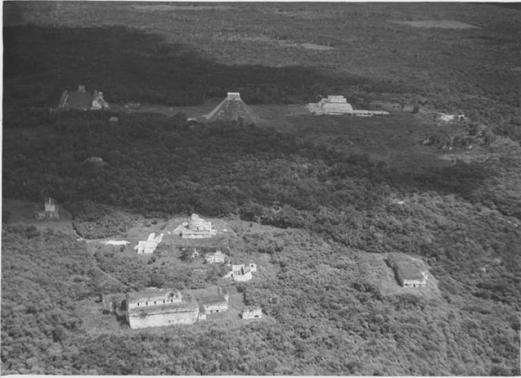 A black and white photograph of tall pyramid like Mayan ruins emerging from a lunch jungle forest.