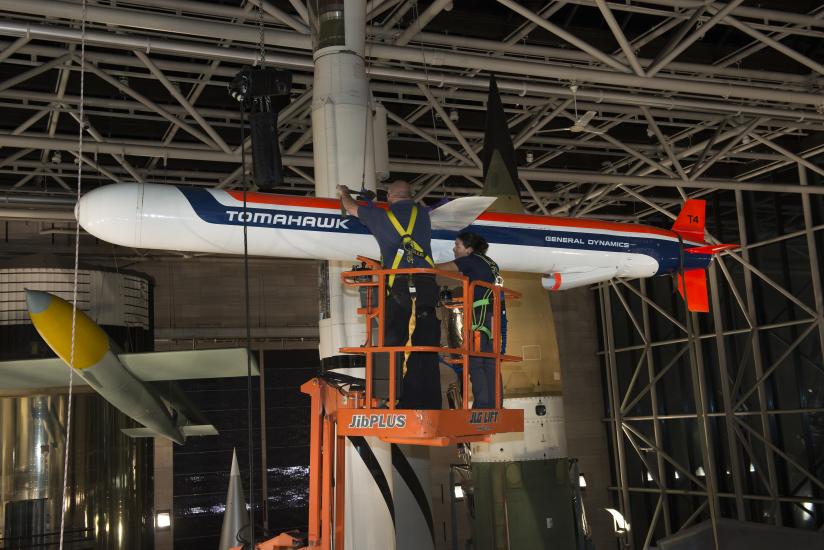 Staff on a lift work to lower a missile attached to the ceiling. 