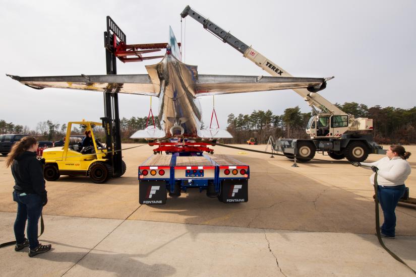 The Douglas DC-3 is being placed on a truck. People are on both sides guiding the process. 