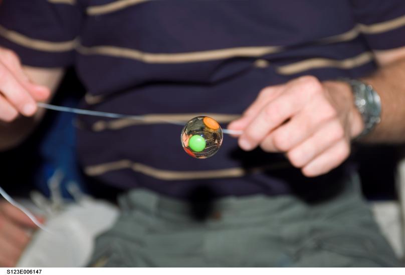 A photo of a water bubble with candy trapped inside floats freely on the middeck of Space Shuttle Endeavour.