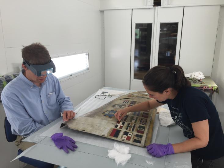 Two conservators work on a airplane cowling. 