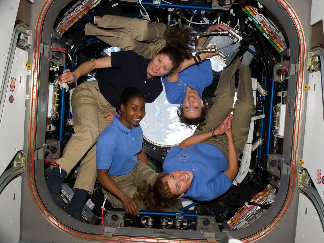 Four women in a space station forming a circular shape to fit in the small room.