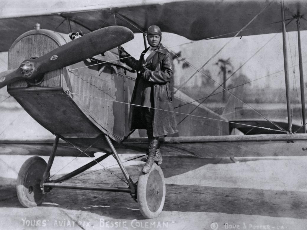 A woman stands on the wing of an airplane.