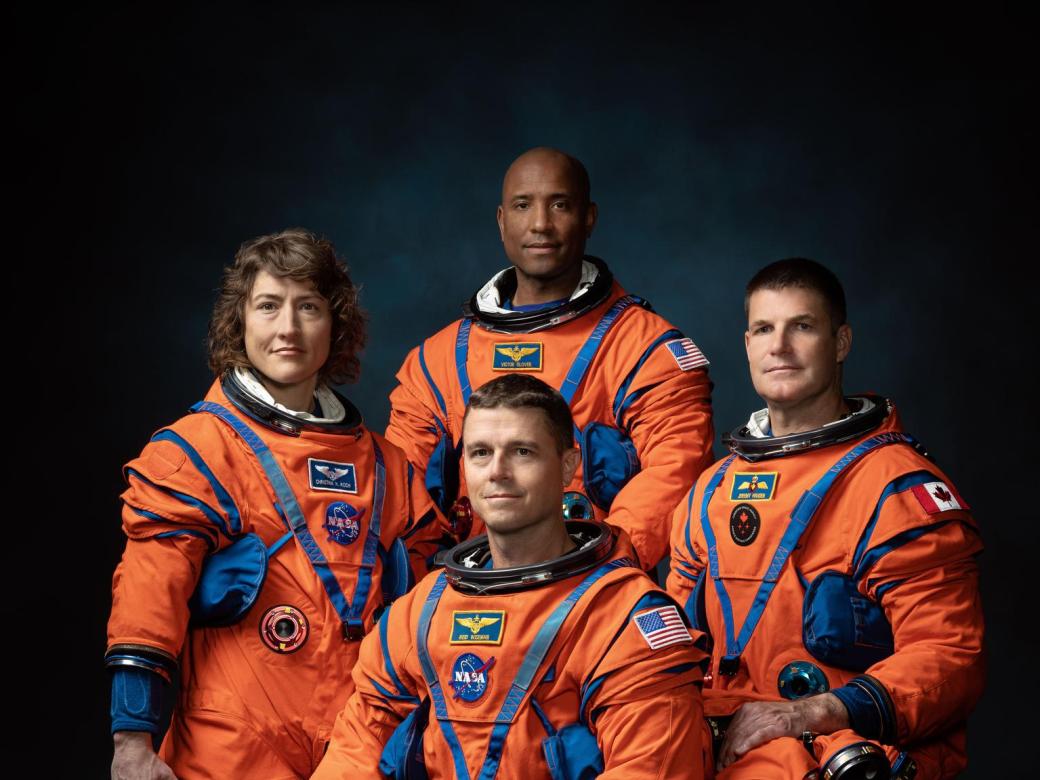 Four astronauts in orange flight suits pose for a photo as a crew.