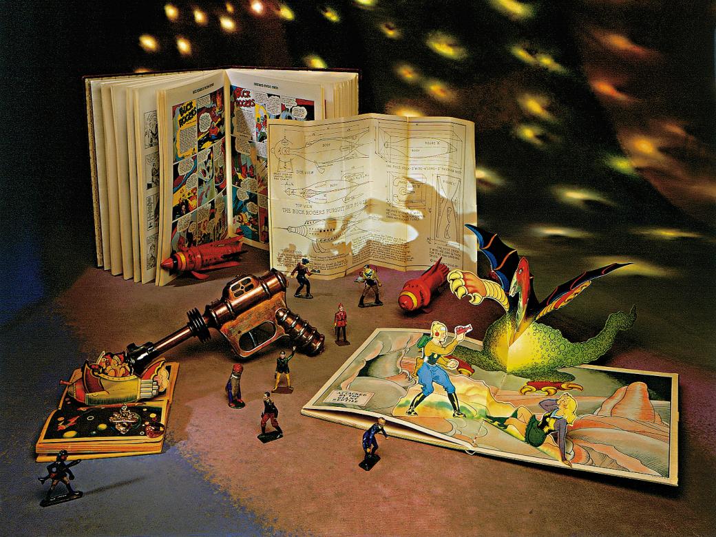 A collection of space-themed toys and comic books on a table with stars projected in the background.